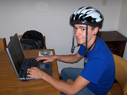 Joven con un casco de bicicleta ante un portátil.