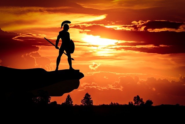 Espartano vestido con armadura en sombra sobre una colina mientras anochece.