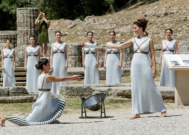 Fotografía con varias mujeres vestidas a la griega que se pasan una antorcha