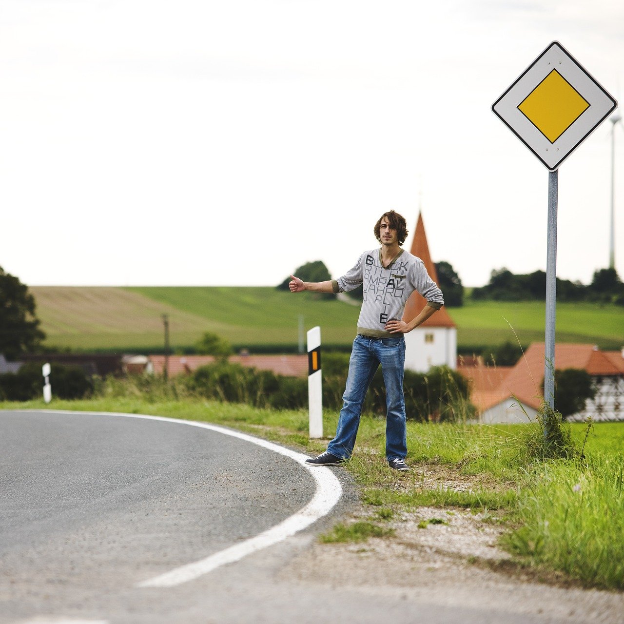 Un joven hace autostop junto a una carretera