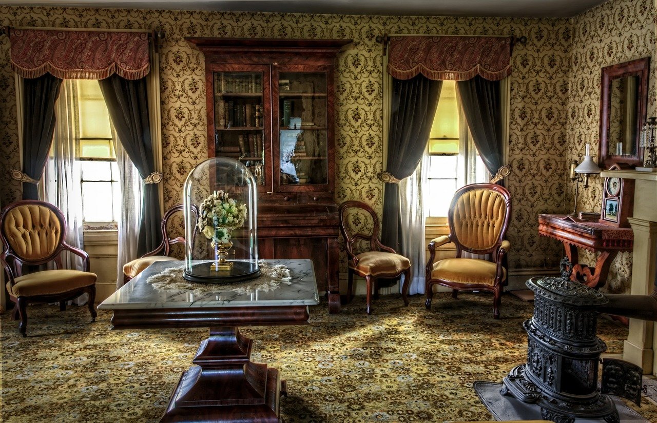 una sala victoriana con 4 butacas clásicas, una mesa central y dos ventanales tapados por cortinas