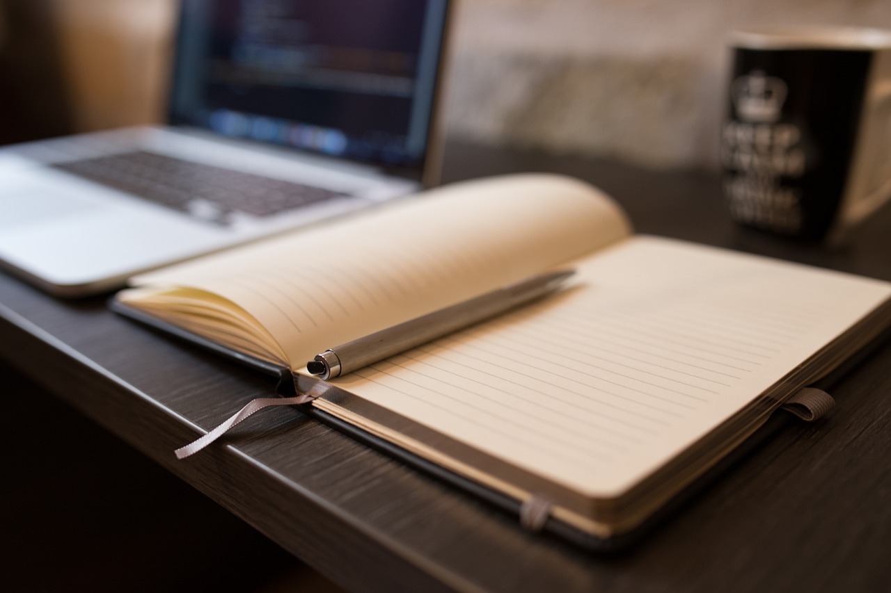 Un cuaderno abierto por la mitad sobre una mesa y sobre él un bolígrafo.