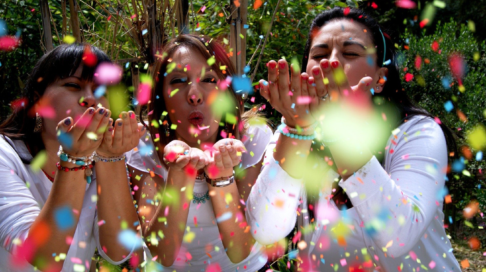 Tres chicas lanzan confetti y sonríen.