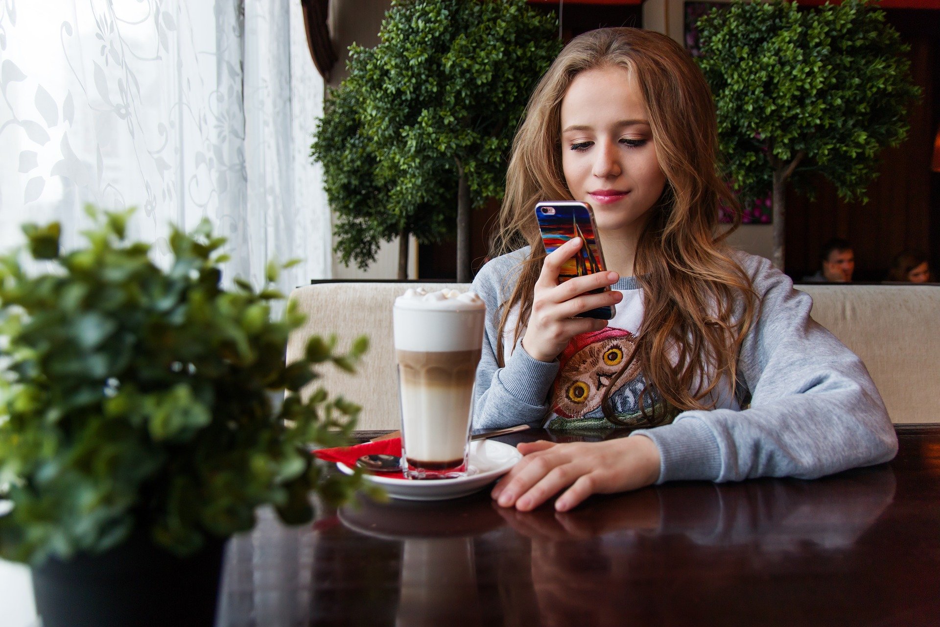 Una adolescente sentada en una cafetería usa su teléfono móvil.