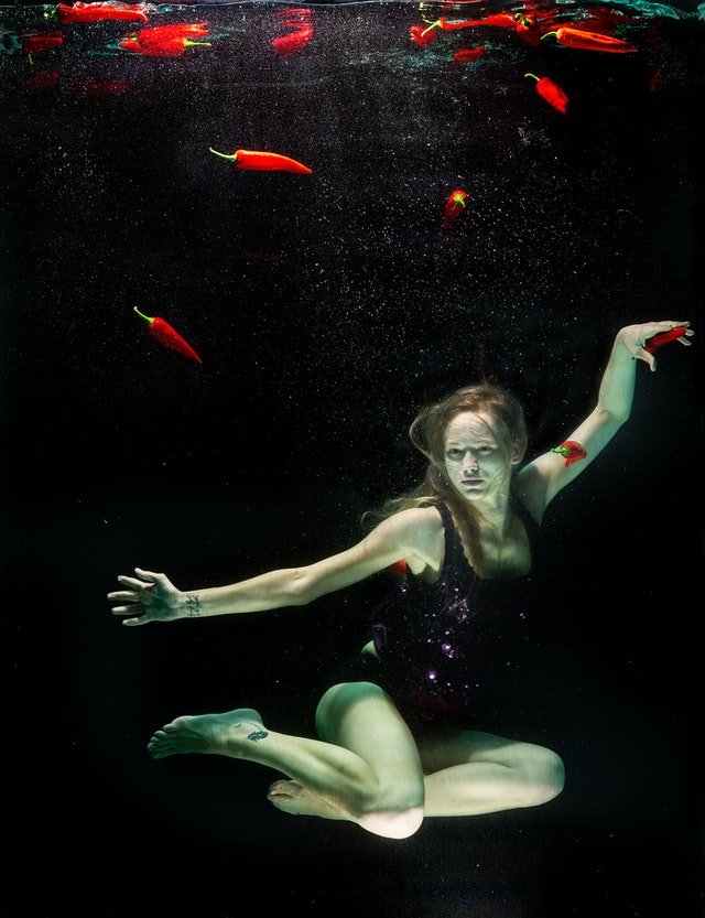 Mujer sumergida en el agua con bañador negro y rodeada de pimientos rojos