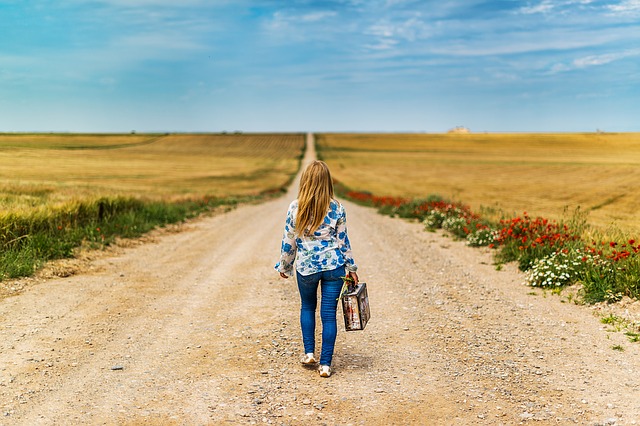 Chica de espaldas con una maleta en un campo abierto. 