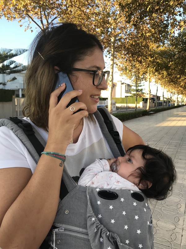 Una chica con un bebé en la mochila hablando con su teléfono móvil.