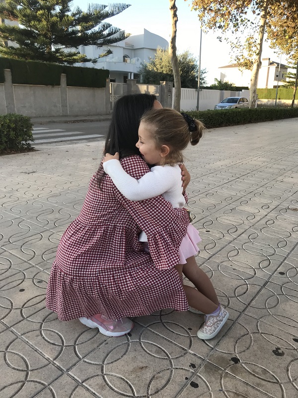 Una chica agachada abrazando a una niña pequeña